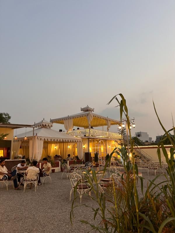 Rajasthani-style tents glowing at dusk in Beanstalk's courtyard, with white iron chairs on gravel.